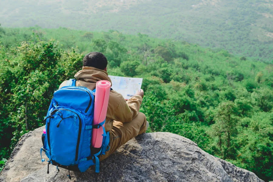 Hiker checking map and backpack on a trail overlook