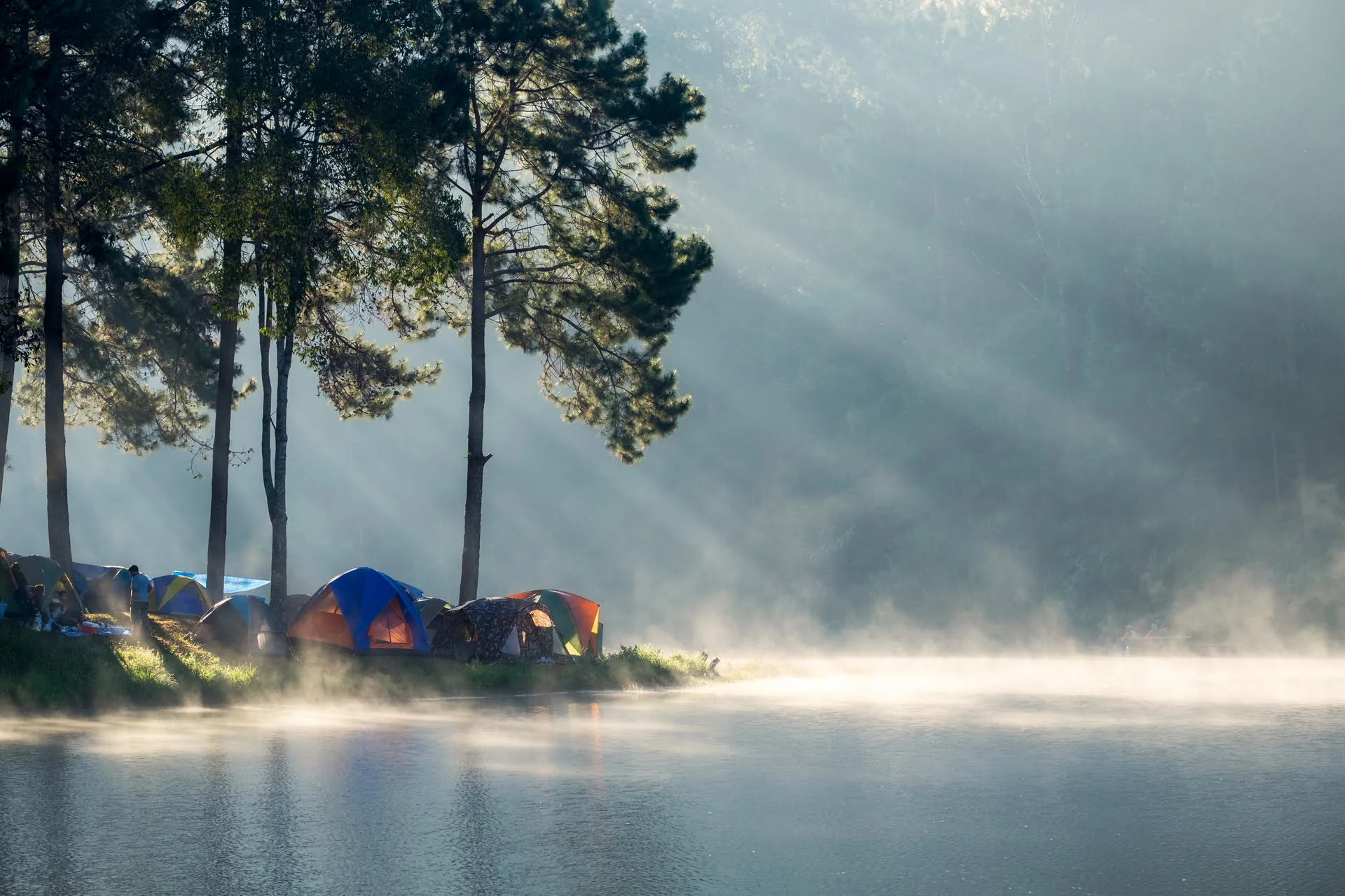 Mountain lake campsite surrounded by forest at sunrise